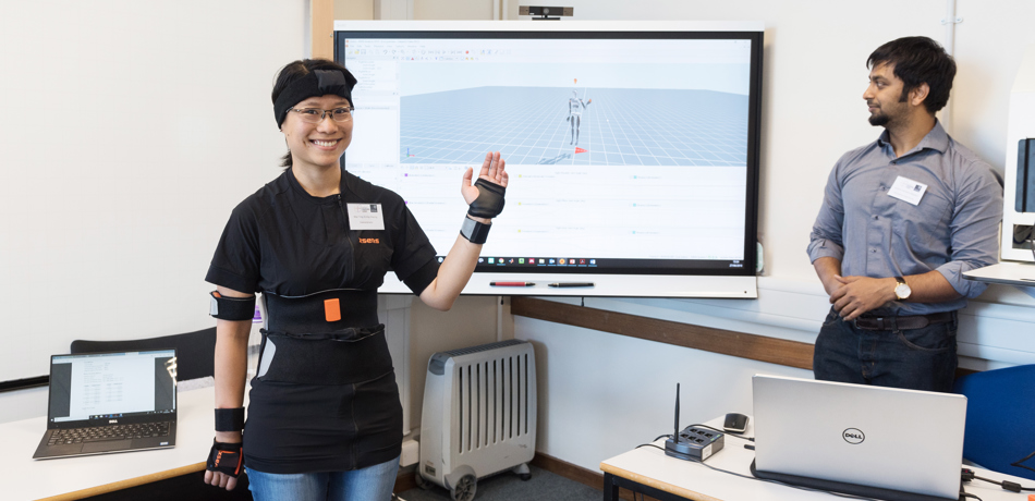 Woman demonstrating a gadget reflecting her actions on a screen behind her.