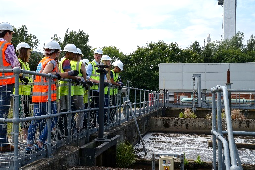 Group of people ona bridge wearing hard hats and high-visibility vests looking at water and pipes