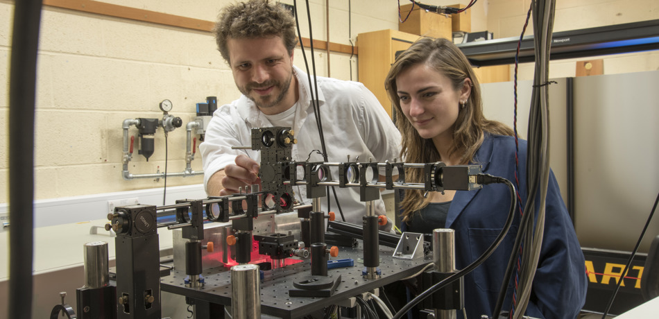 Two postgraduate students looking at a large piece of electrical engineering