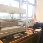 Student in lab coat using a stress testing machine on a bar of metal