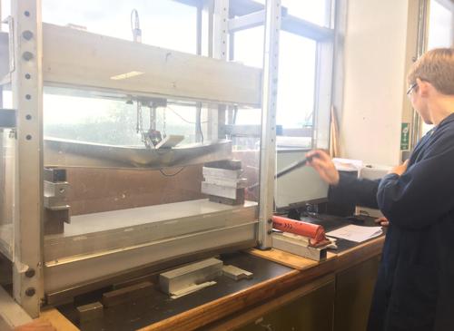 Student in lab coat using a stress testing machine on a bar of metal