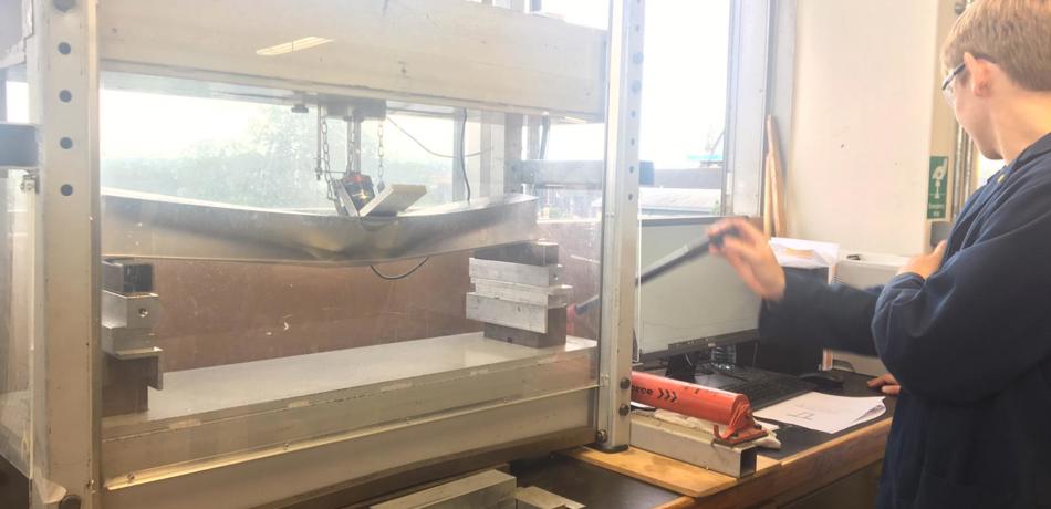 Student in lab coat using a stress testing machine on a bar of metal