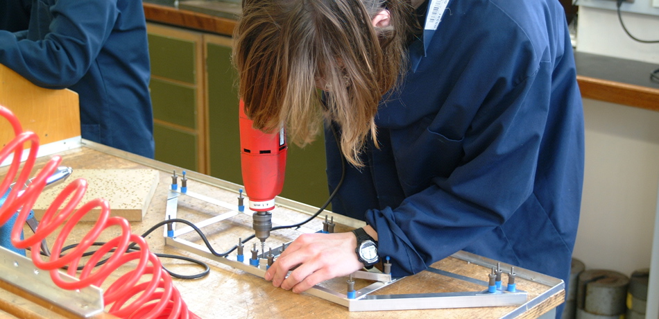 Student drilling into a metal frame bridge