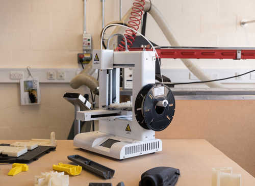 Tabletop 3D printer surrounded by plastic products
