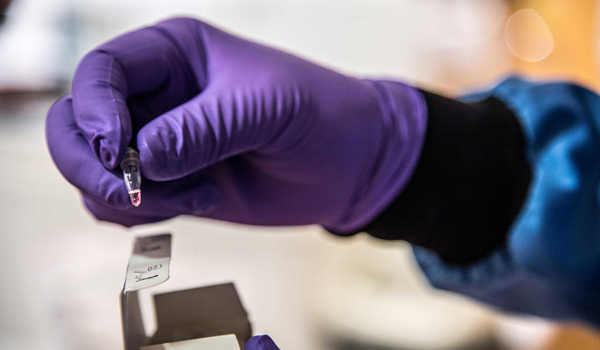Researcher wearing PPE holding a vial of coronavirus sample